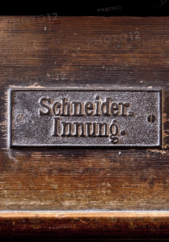 Permanently mounted sign of the tailors' guild on the church pew in the Nikolaikirche