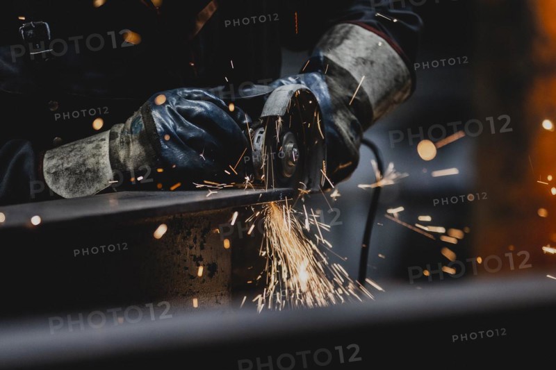 A metal worker works on a steel beam with a cut-off grinder