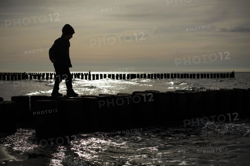 Symbolic photo on the subject of children's fear. A child balances on wooden stilts over the water. Arenshoop
