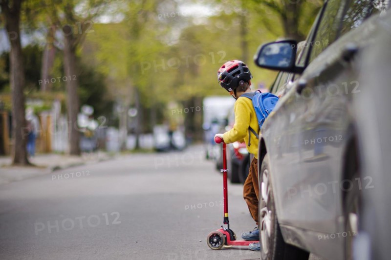 Symbolic photo on the subject of children in road traffic A little boy stands with his scooter between parked cars on a street. Berlin