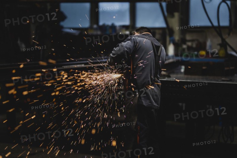 A metal worker works on a steel beam with a cut-off grinder