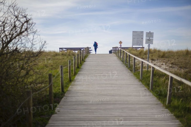 A woman with a child in her arms walks across a beach access on the Fischland-Darss-Zingst peninsula in Mecklenburg-Western Pomerania. Arenshoop