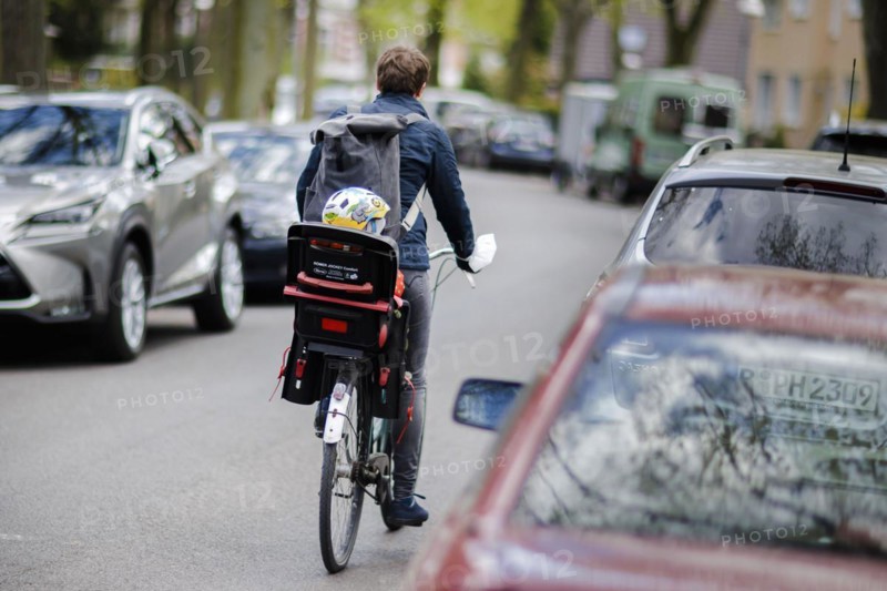 Symbolic photo on the subject of children in road traffic A toddler is sitting in a child seat on a bicycle and is being driven across a road by his mother. Berlin