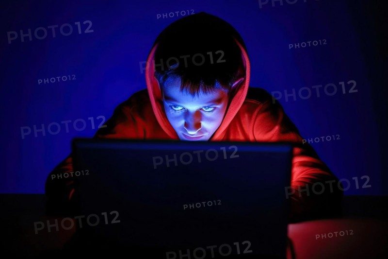 A teenager about 13 years old sits at his laptop at night