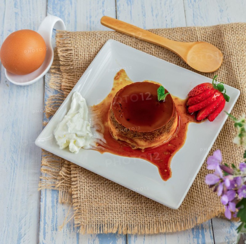 Egg custard with cream and strawberries on a white plate on a blue wooden table with flowers