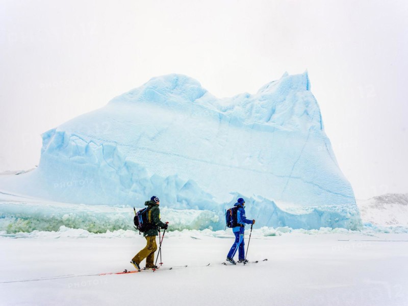 Ski tourers in front of iceberg in frozen Kong Oscar Fjord