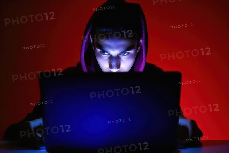 A young man in his mid-20s works at his laptop at night