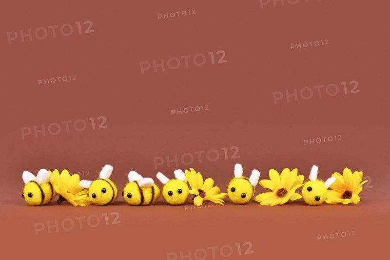 Felt bees and yellow flowers in a row on brown background with copy space