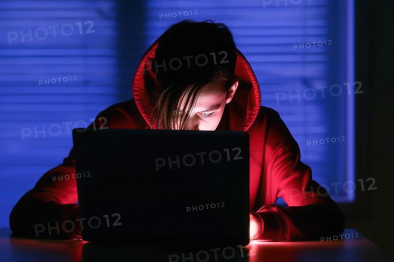 A young person in his mid-20s works at a laptop at night