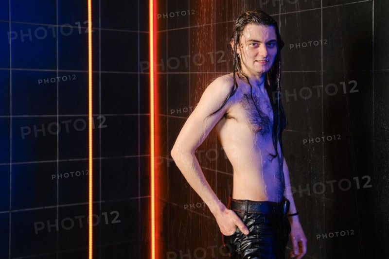 Cheerful man with long hair posing under water jets in shower with neon light