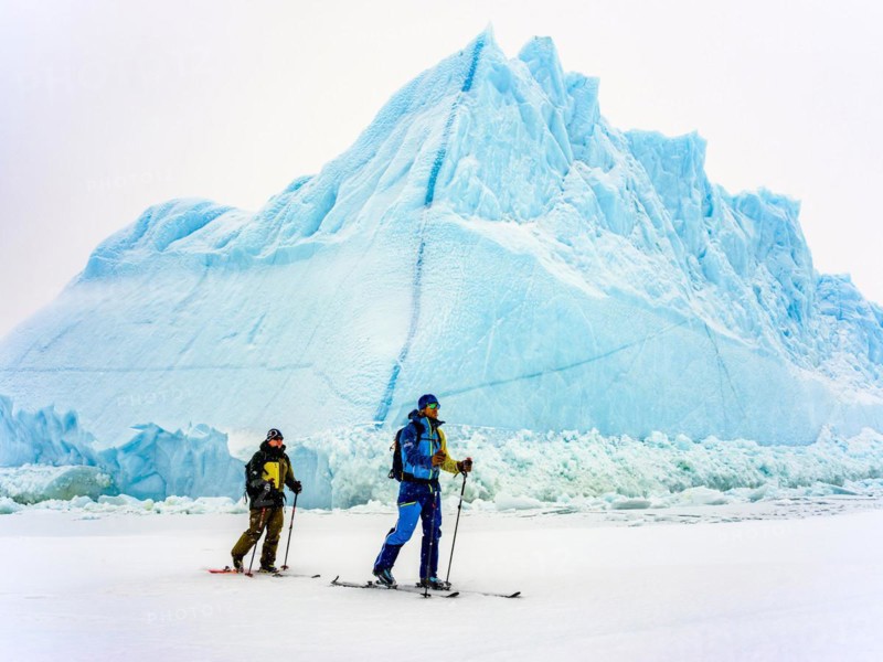 Ski tourers in front of iceberg in frozen Kong Oscar Fjord
