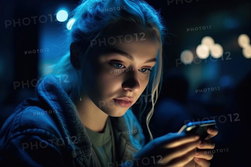 A fifteen year old girl with blonde hair looks at her mobile phone at night