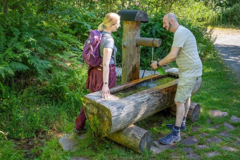 Hiking couple filling drinking bottle at the wooden fountain on the hiking trail Sprollenhaeuser Hut