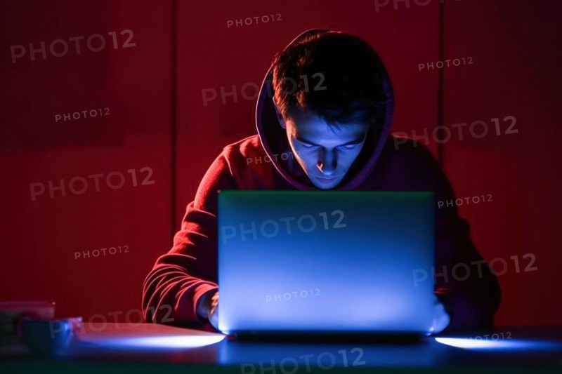A young man in his mid-20s works at his laptop at night
