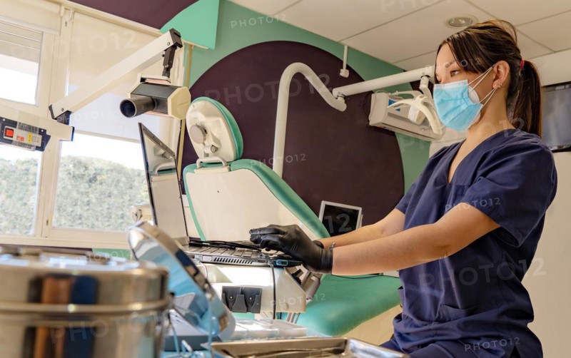 Young doctor wearing a mask works on the computer in her dental office