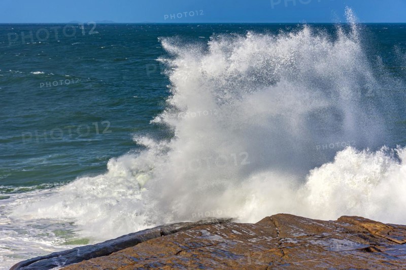 Wave breaking over rocks with water splashing with blue sky on a rough sea day in Rio de Janeiro
