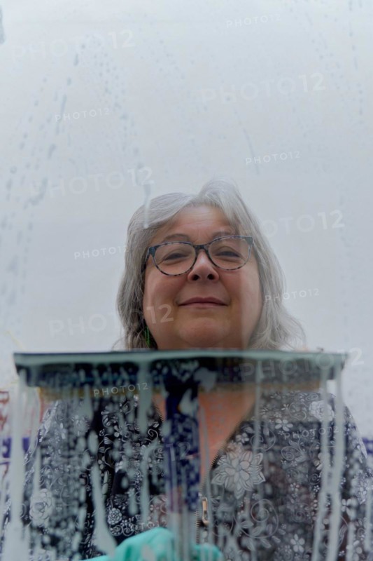 Close-up of a white-haired woman cleaning soap-covered windows with a squeegee