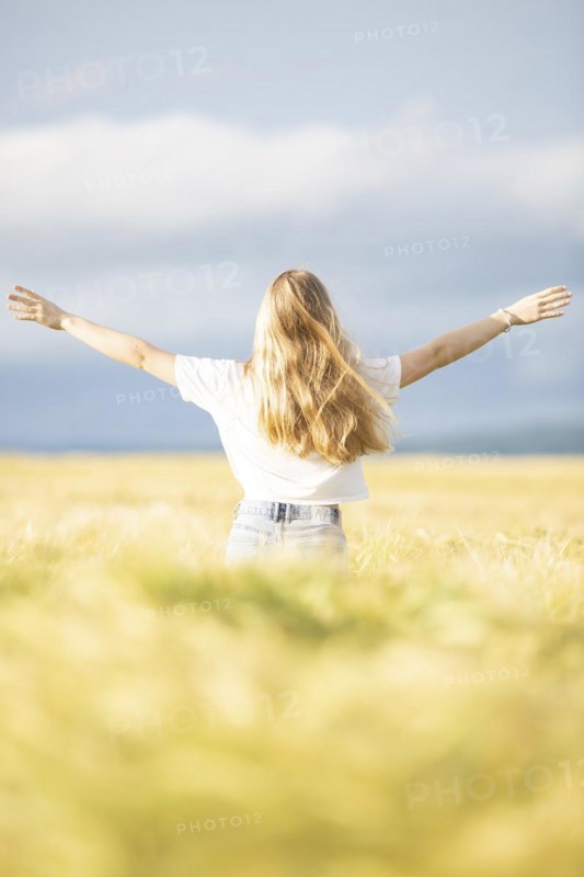 A young girl walks through a cornfield on a sunny warm day and spreads out her arms