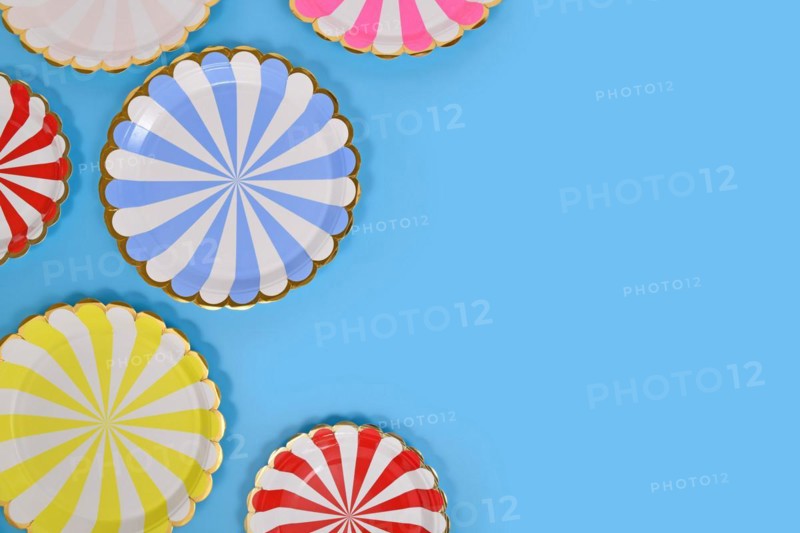 Colorful striped paper party plates on side of blue background with copy space