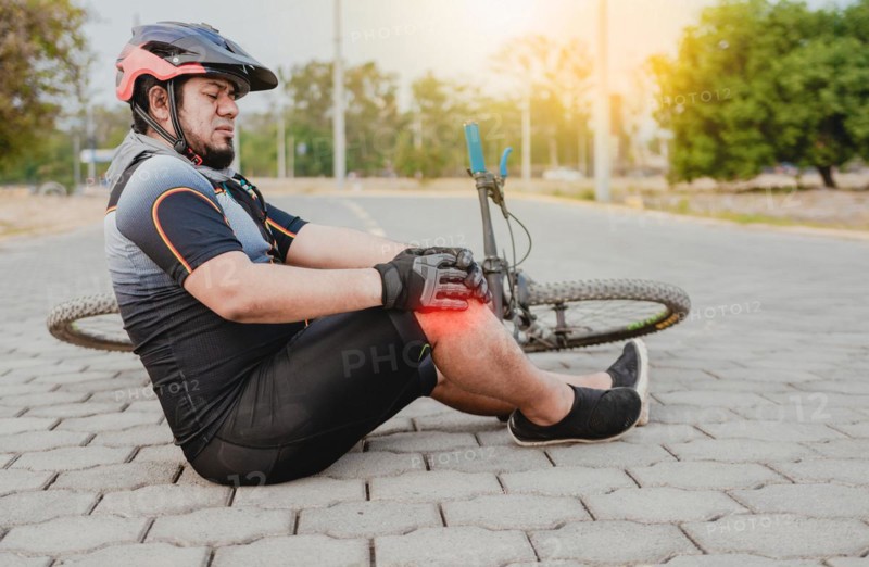 Cyclist with knee pain outdoors. Male cyclist sitting on the pavement with knee pain. Concept of a cyclist with knee injury outdoors