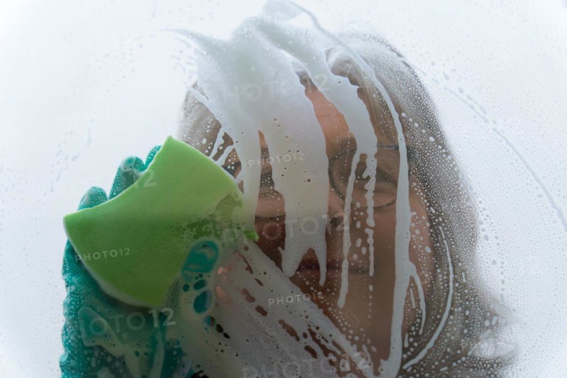 Closeup a woman cleans the glass with a green sponge and gloves