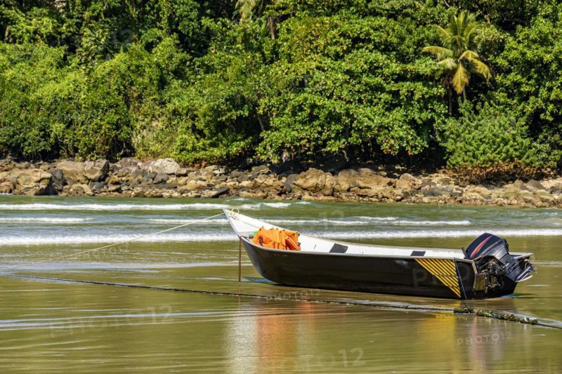 Speedboat standing on the sand of the beach with the rocks and rainforest in the background on a sunny day in Bertioga on the coast of the state of Sao Paulo