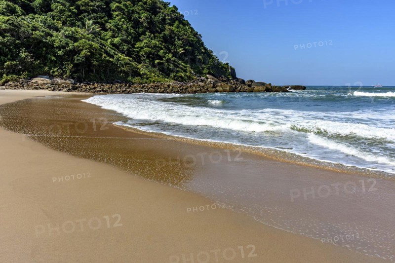Paradisiacal rocky beach with clean and calm waters surrounded by forest and hills in Bertioga coast of Sao Paulo state