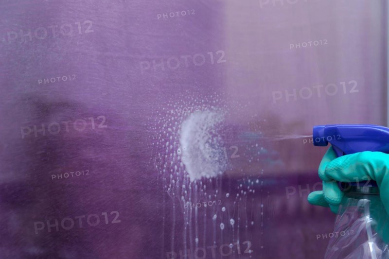 Close-up shot of a spray can of spray cleaner spraying liquid onto a glass pane