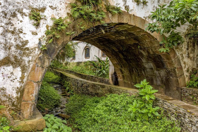 Old historical stone tunnel passing through vegetation and old colonial-style houses in the historic city of Ouro Preto in the state of Minas Gerais.