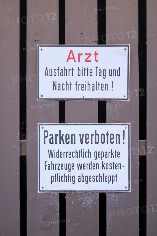 Signs doctor. Exit please keep clear day and night! and Parking prohibited! Illegally parked vehicles will be towed away for a fee mounted on brown painted wooden slats