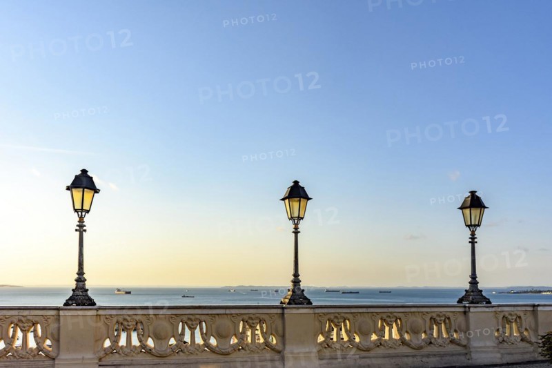 Old colonial style lanterns lighting on walls in the streets of Salvador with the All Saints bay in the background with their boats during the sunset