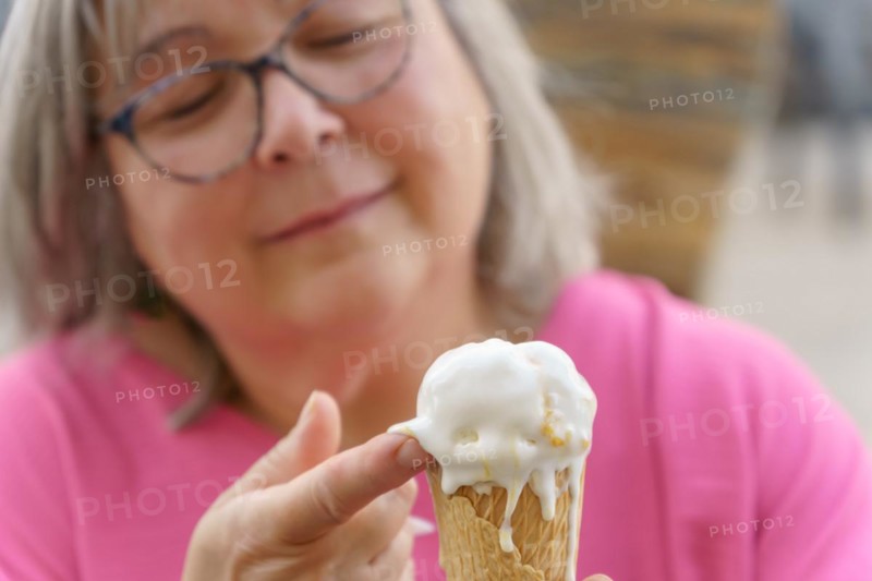 Close-up of a white-haired woman with glasses eating an ice cream with her fingers