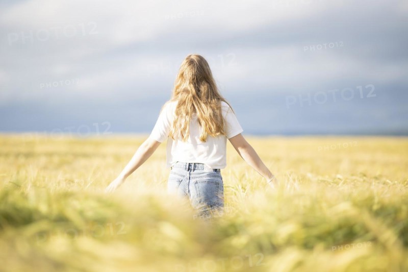 A young girl walks through a cornfield on a sunny warm day and spreads out her arms