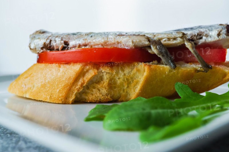 Tapa of sardines on a slice of bread with tomato and olives on a white plate with a typical spanish white background