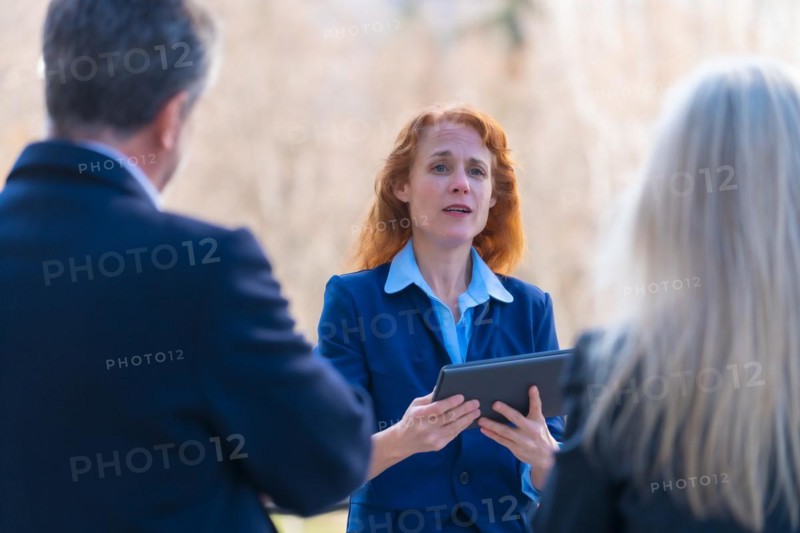 Collaborative and Innovative Red-Haired Female Business Professional Engaging in Teamwork with Colleagues through Digital Tablet while Participating in a Remote Business Meeting in a Modern Office Environment