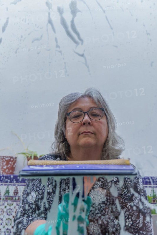 Close-up of a white-haired woman cleaning soap-covered windows with a squeegee
