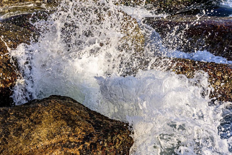 Water and sea foam splashing in the air with waves crashing against rocks