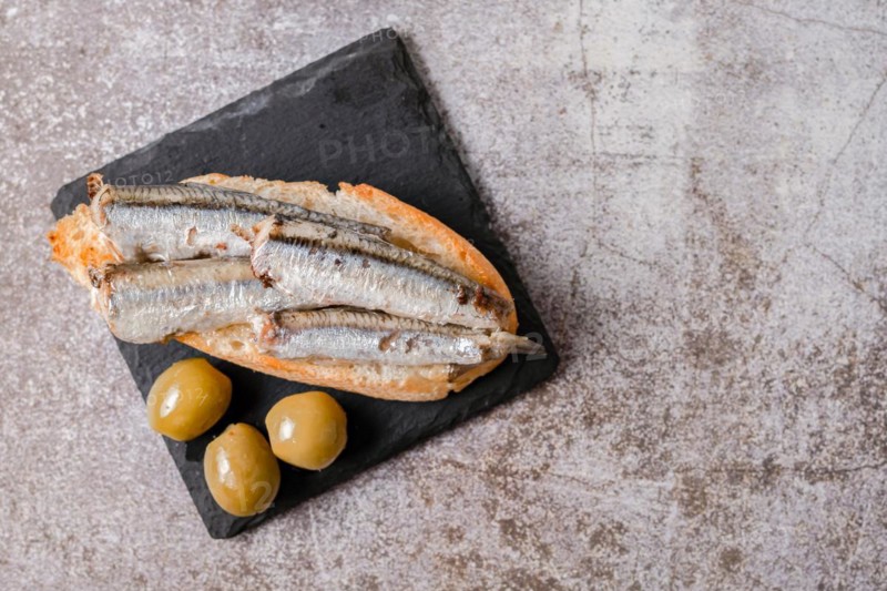 Tapa of sardines on a slice of bread with tomato and olives on black slate typical Spanish