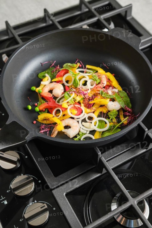 Frying fresh vegetables and shrimps in a frying pan
