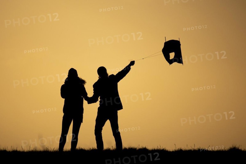 The silhouette of two people is silhouetted while flying a kite in front of sunset in Berlin