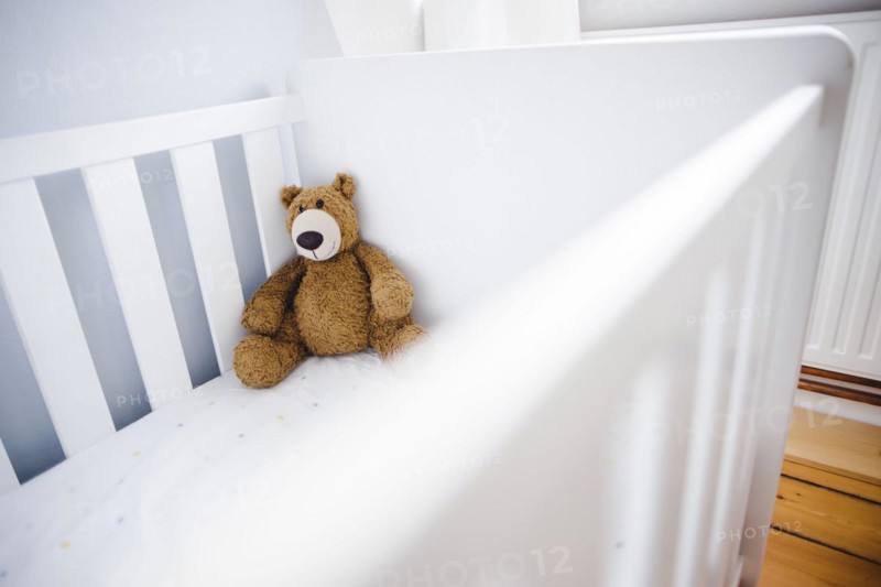 Symbolic photo on the subject of wanting a child. A teddy bear sits in an empty cot. Berlin