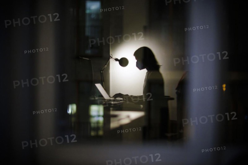 Symbolic photo on the subject of masks at the workplace. A woman sits in her desk in the office in the evening wearing an FFP2 mask. Berlin