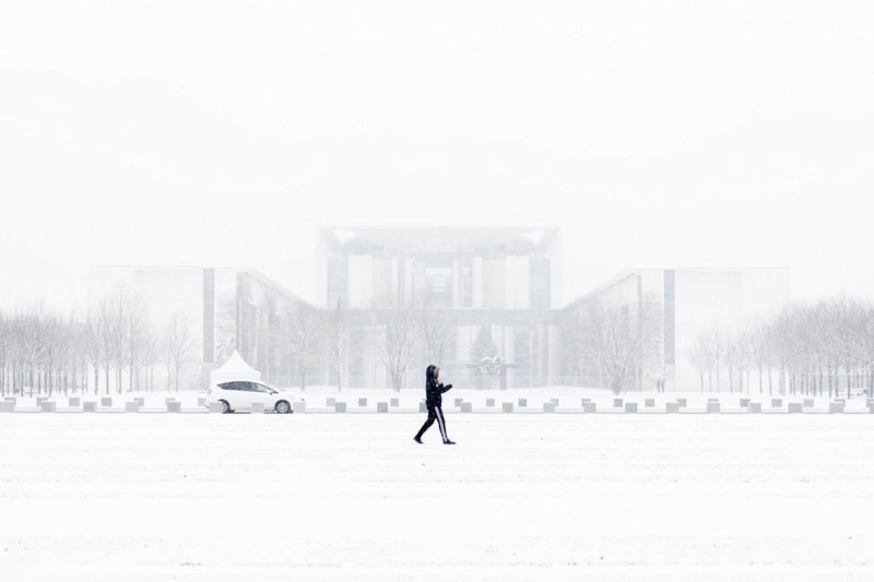 A person is silhouetted in front of the Chancellery in the driving snow in Berlin