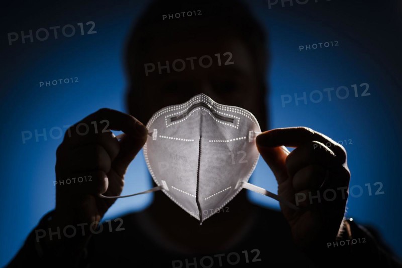 A man holds an FFP2 protective mask in front of his face. Berlin