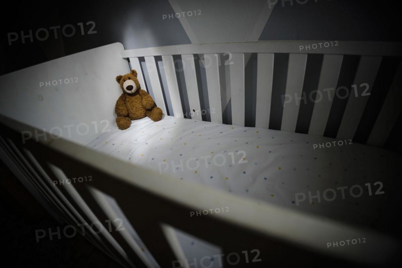 Symbolic photo on the subject of child abuse. A teddy bear sits in an empty cot. Berlin