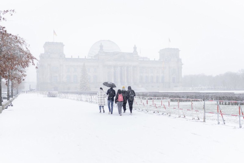 Five people stand in front of the Bundestag in the driving snow in Berlin