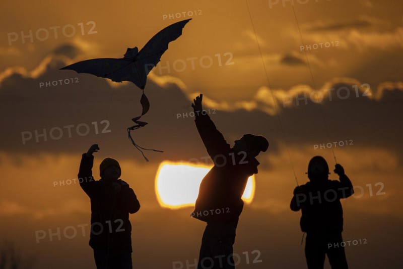The silhouette of three people emerges while flying a kite in front of sunset in Berlin