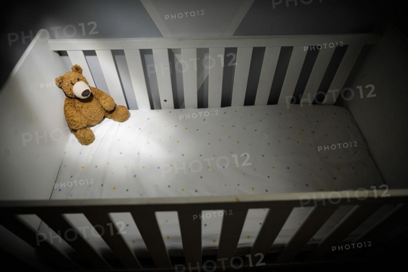 Symbolic photo on the subject of child abuse. A teddy bear sits in an empty cot. Berlin