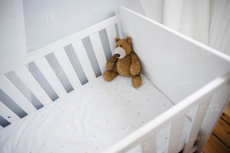 Symbolic photo on the subject of wanting a child. A teddy bear sits in an empty cot. Berlin