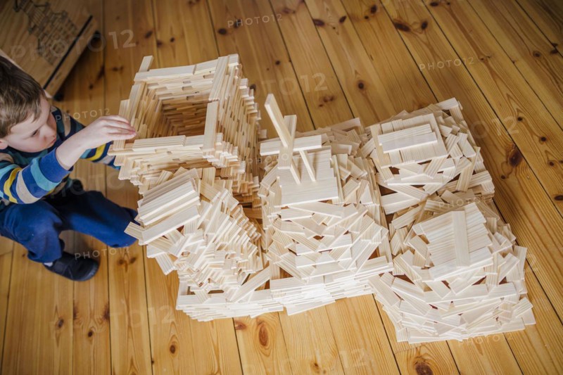 Symbolic photo on the subject of creative play among children. A boy builds with wooden building blocks. Berlin